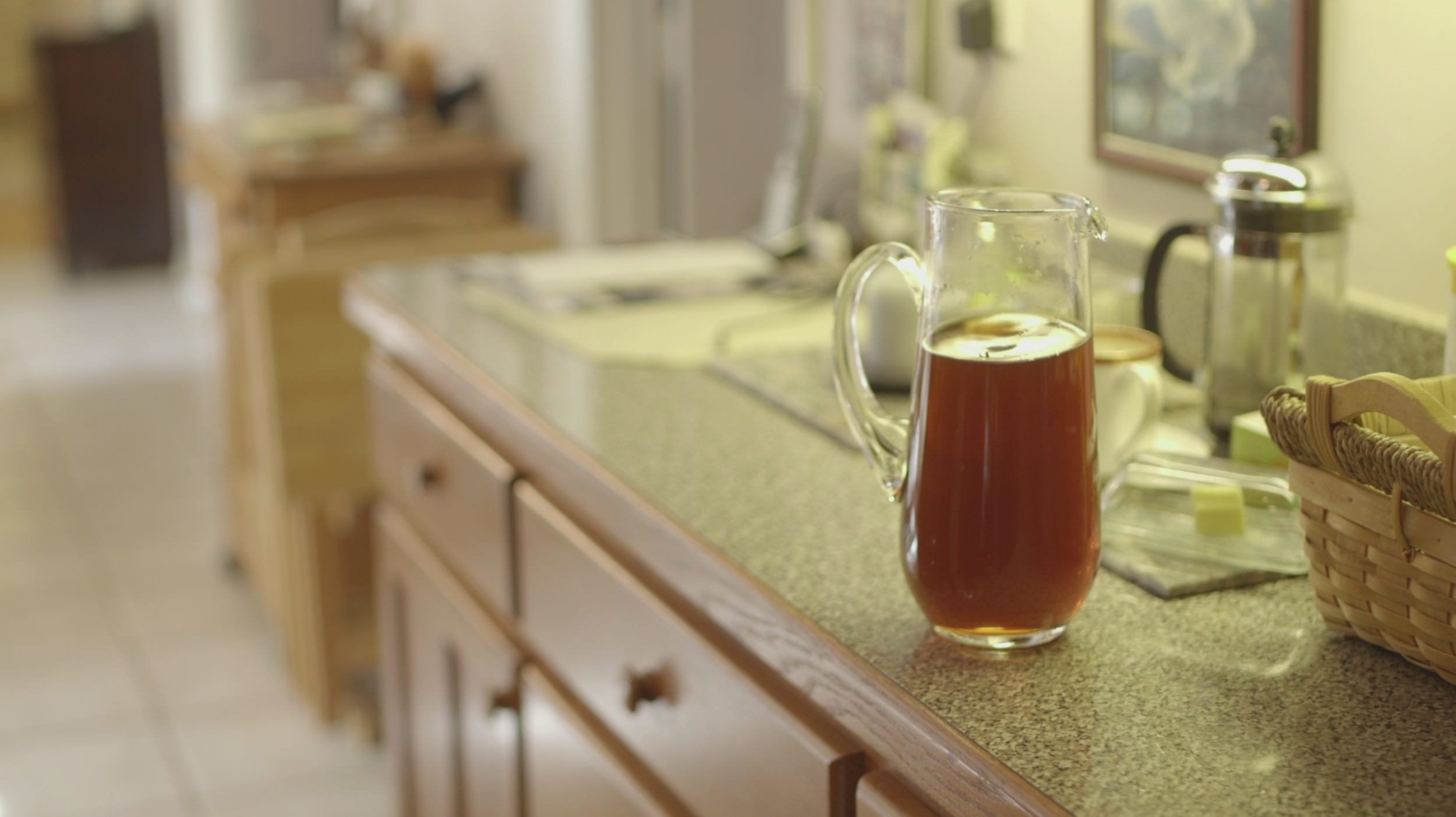 A glass pitcher filled with sweet tea on a laminate counter, with other kitchen items blurred in the background.
