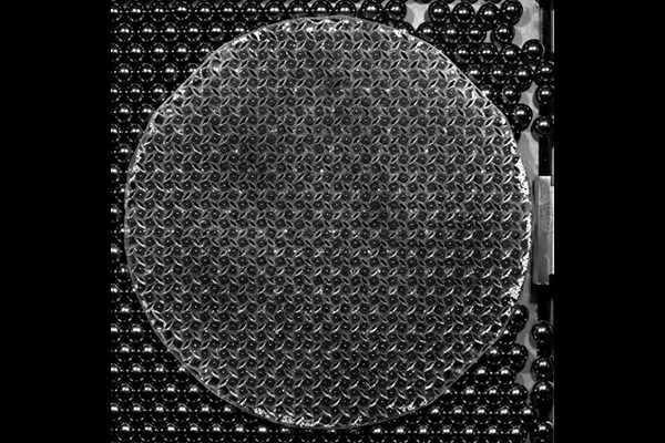 a round disk making a slow-motion wave over a field of small metal balls