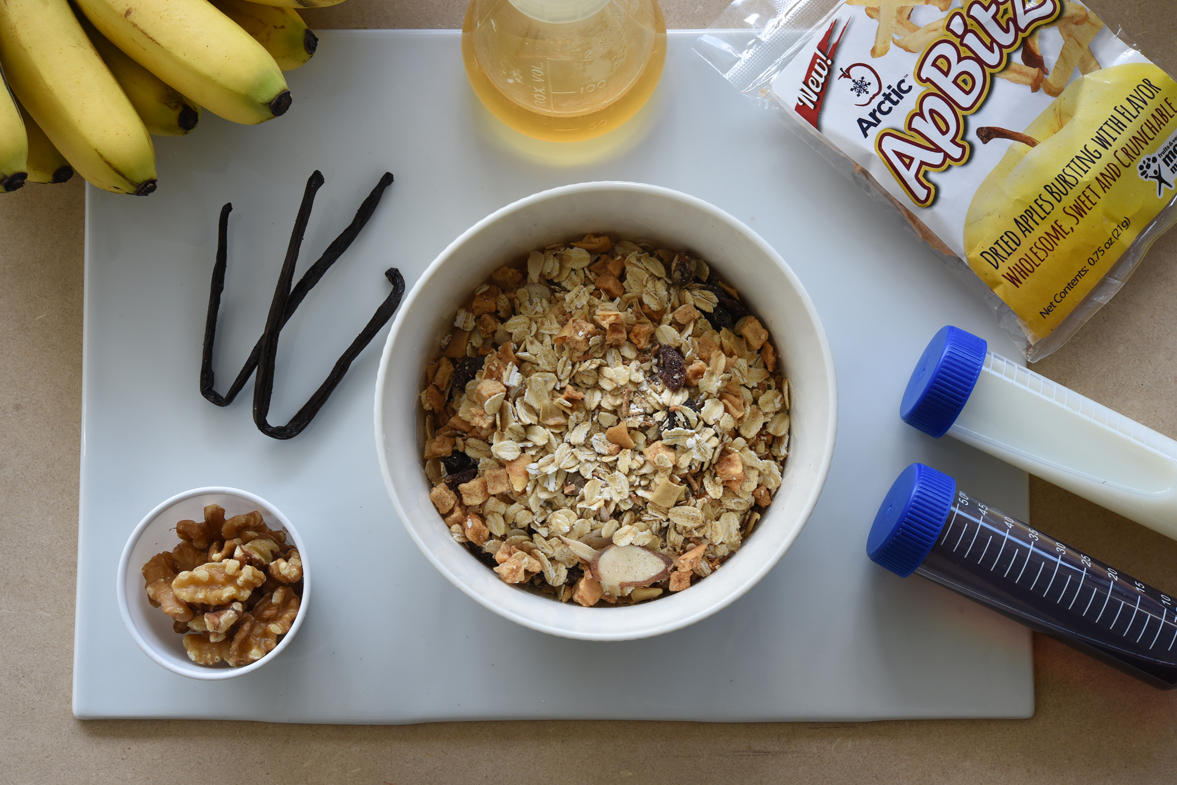 Oats surrounded by bananas, apple bites, pecans, and milk