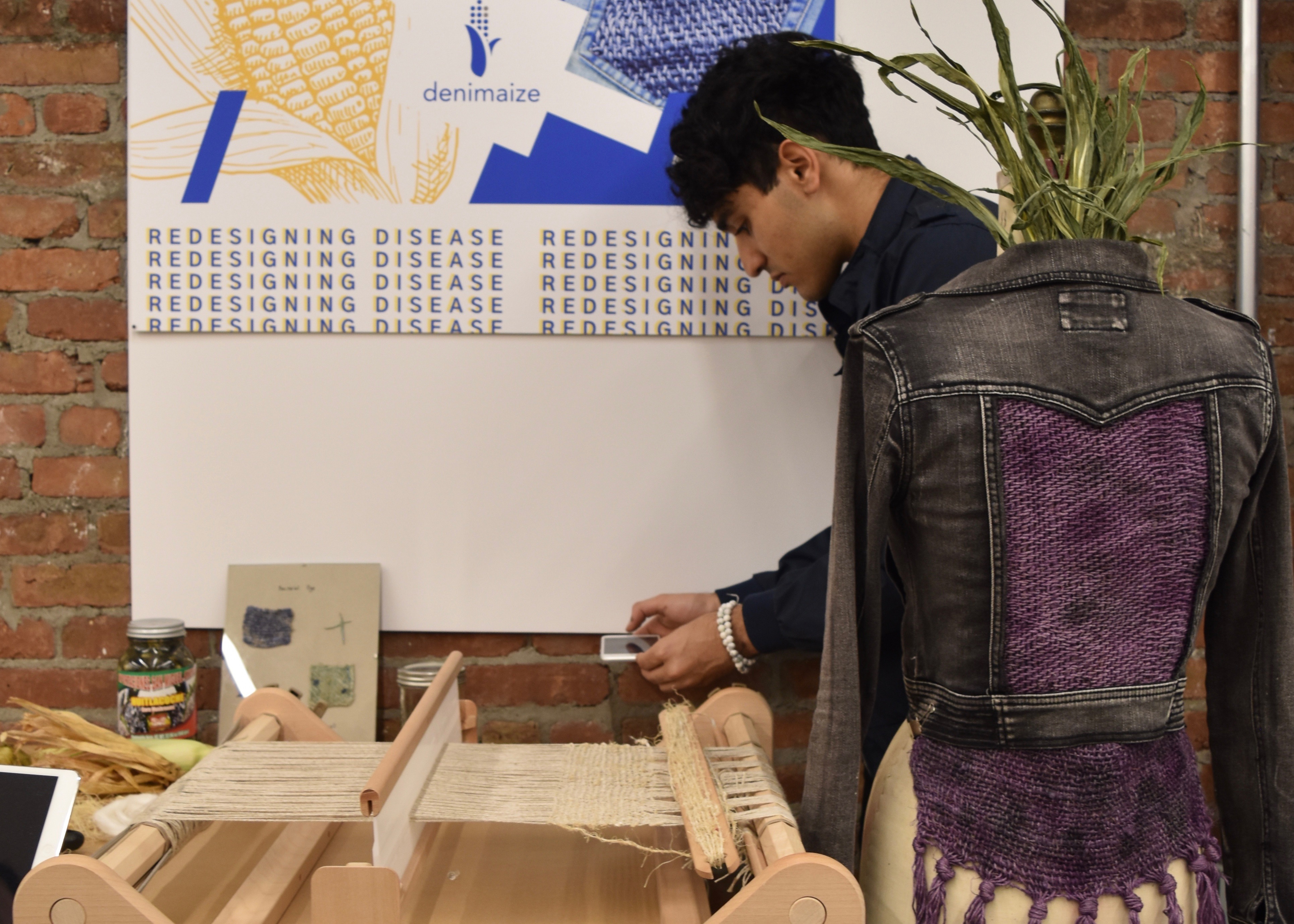 student setting up design exhibit with a jacket and a loom and a sign. 