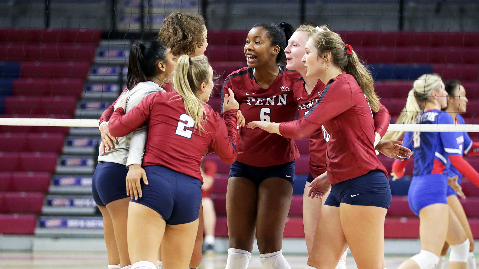 Members of the women's volleyball team converse on the court in a circle.