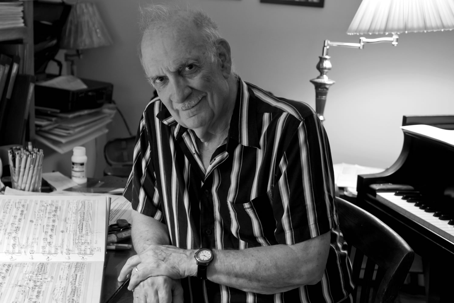 George Crumb sitting next to a piano with a hand-notated musical score in front of him. 