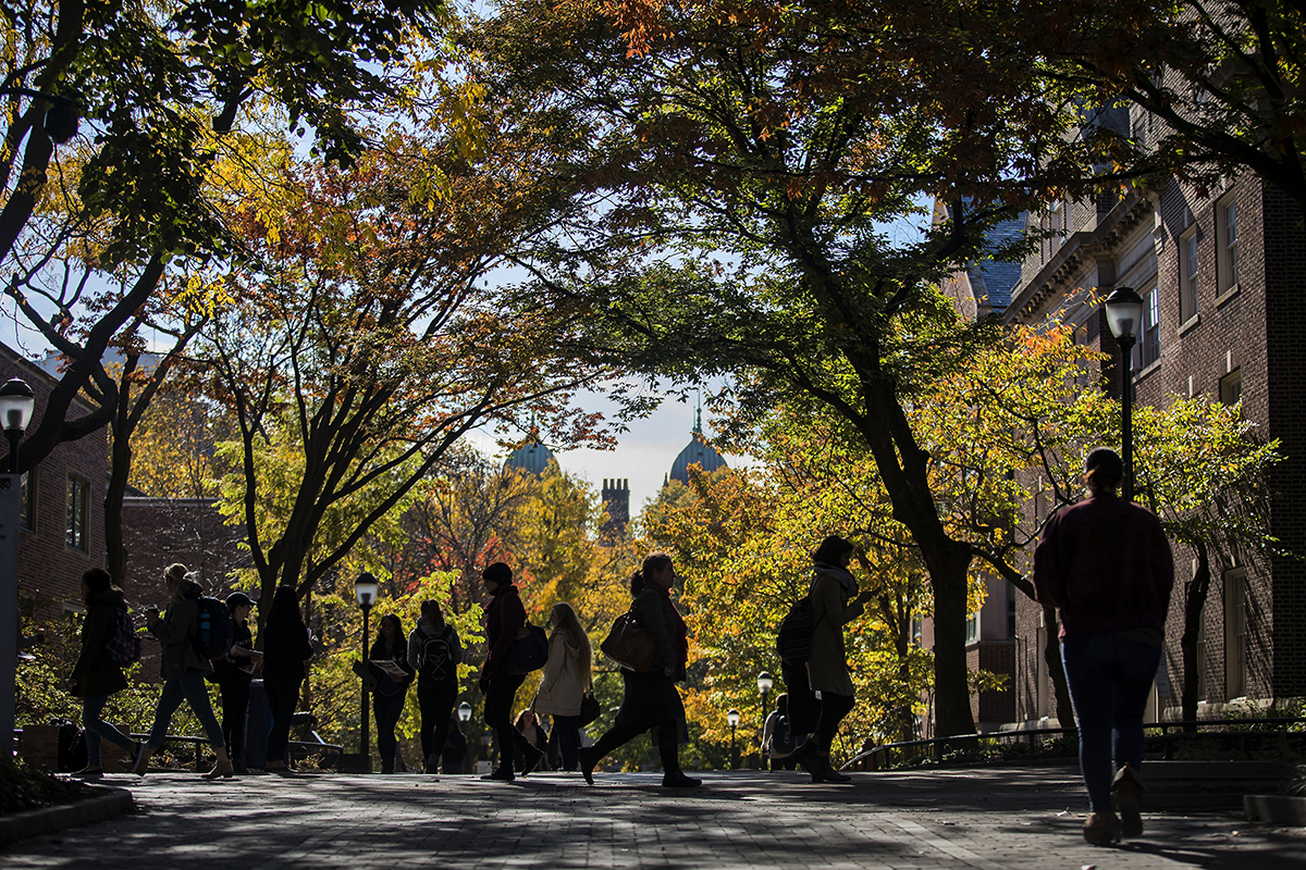 Pedestrians on Penn campus in the autumn sun with fall leaves.
