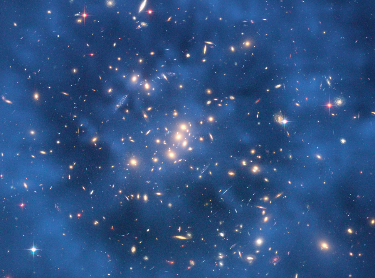 a cluster of galaxies shown against a dark blue background, a faint darker ring can be seen around the center of the image