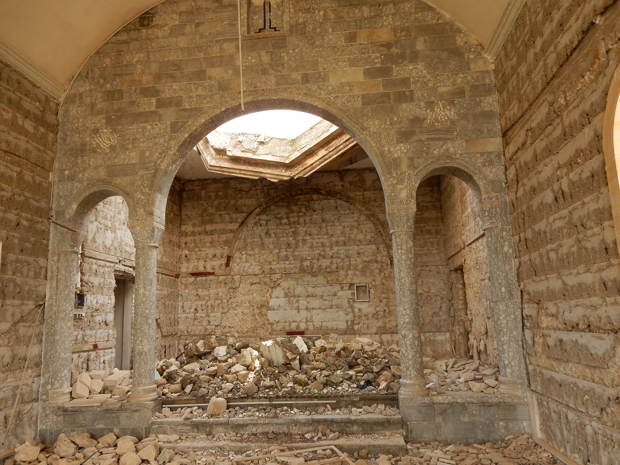An ancient brick structure with a caved-in roof and rubble on the ground shot from outside an indoor archway.