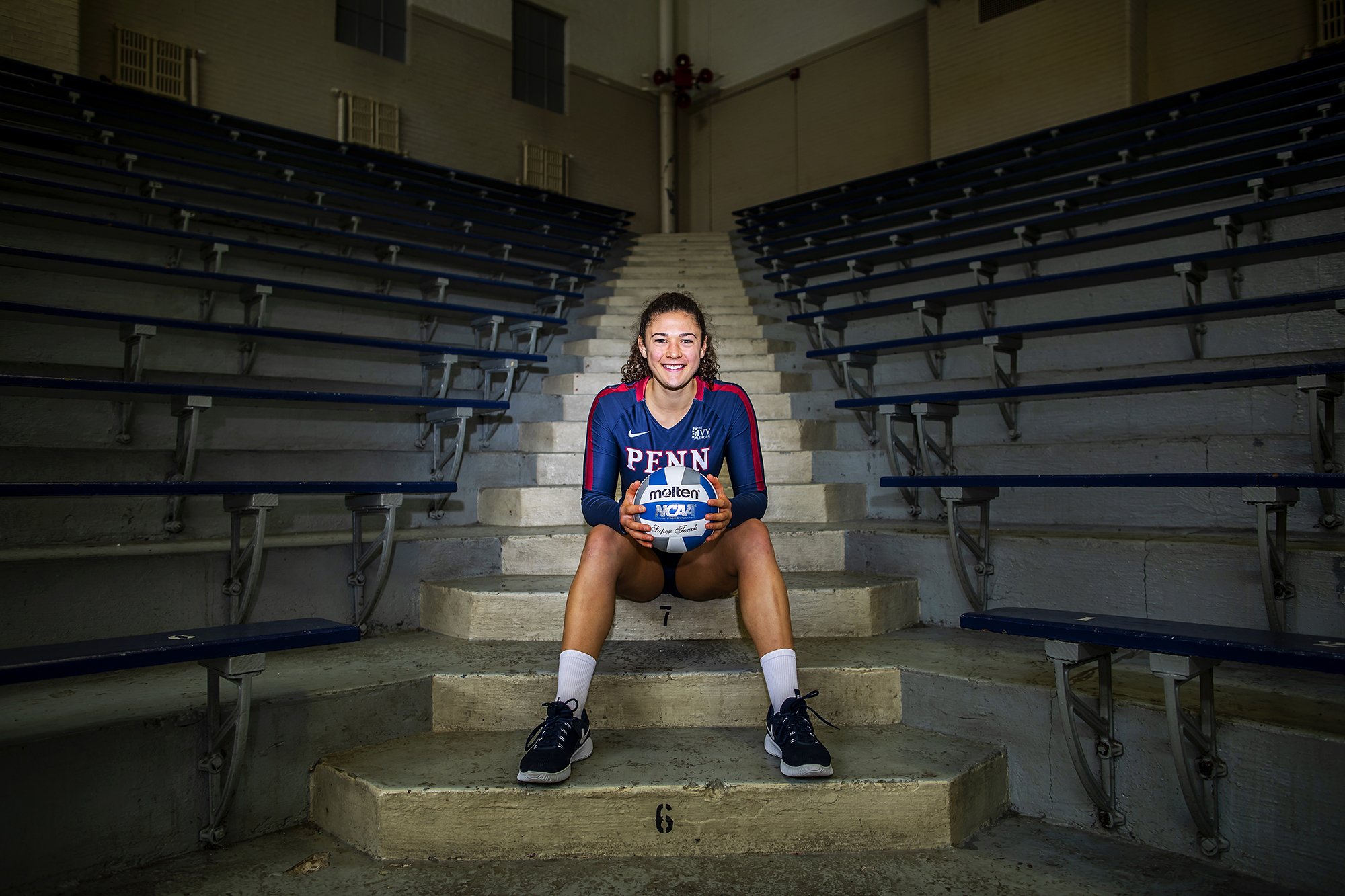 Parker Jones sits on the steps at the Palestra holding a volleyball. 