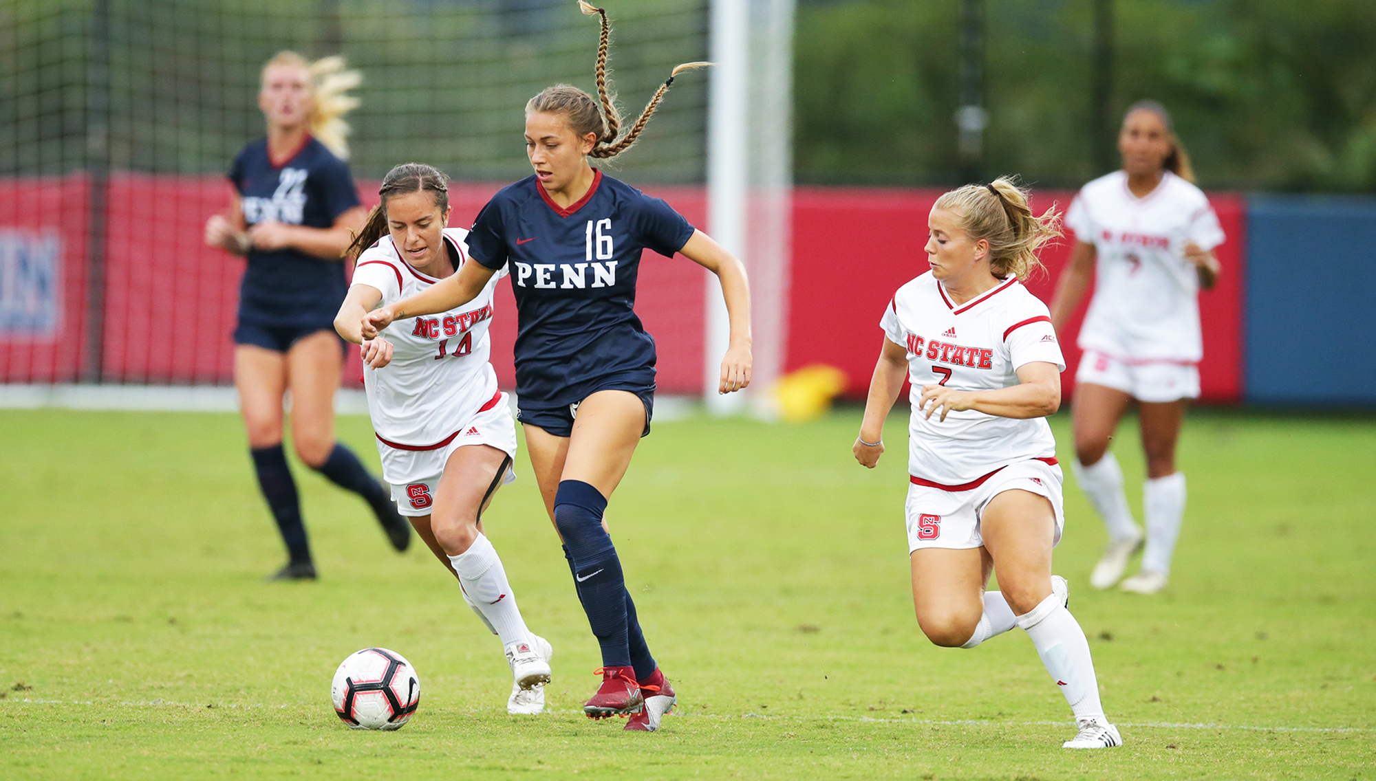 Breukelen Woodard of the women's soccer team moves with the ball between two NC State defenders.