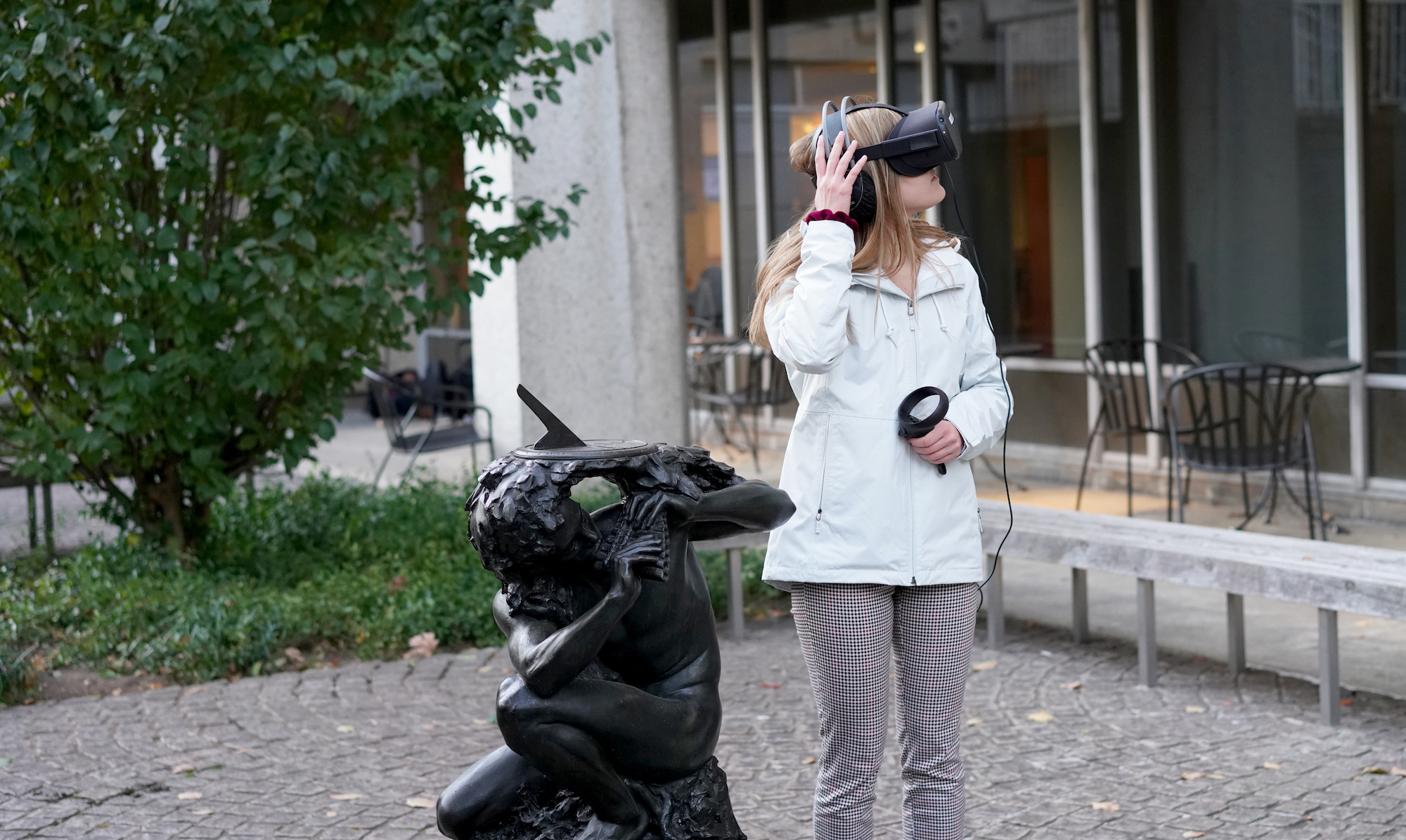 Person wearing a virtual reality headset looks to the side, standing next to a statue facing the same direction