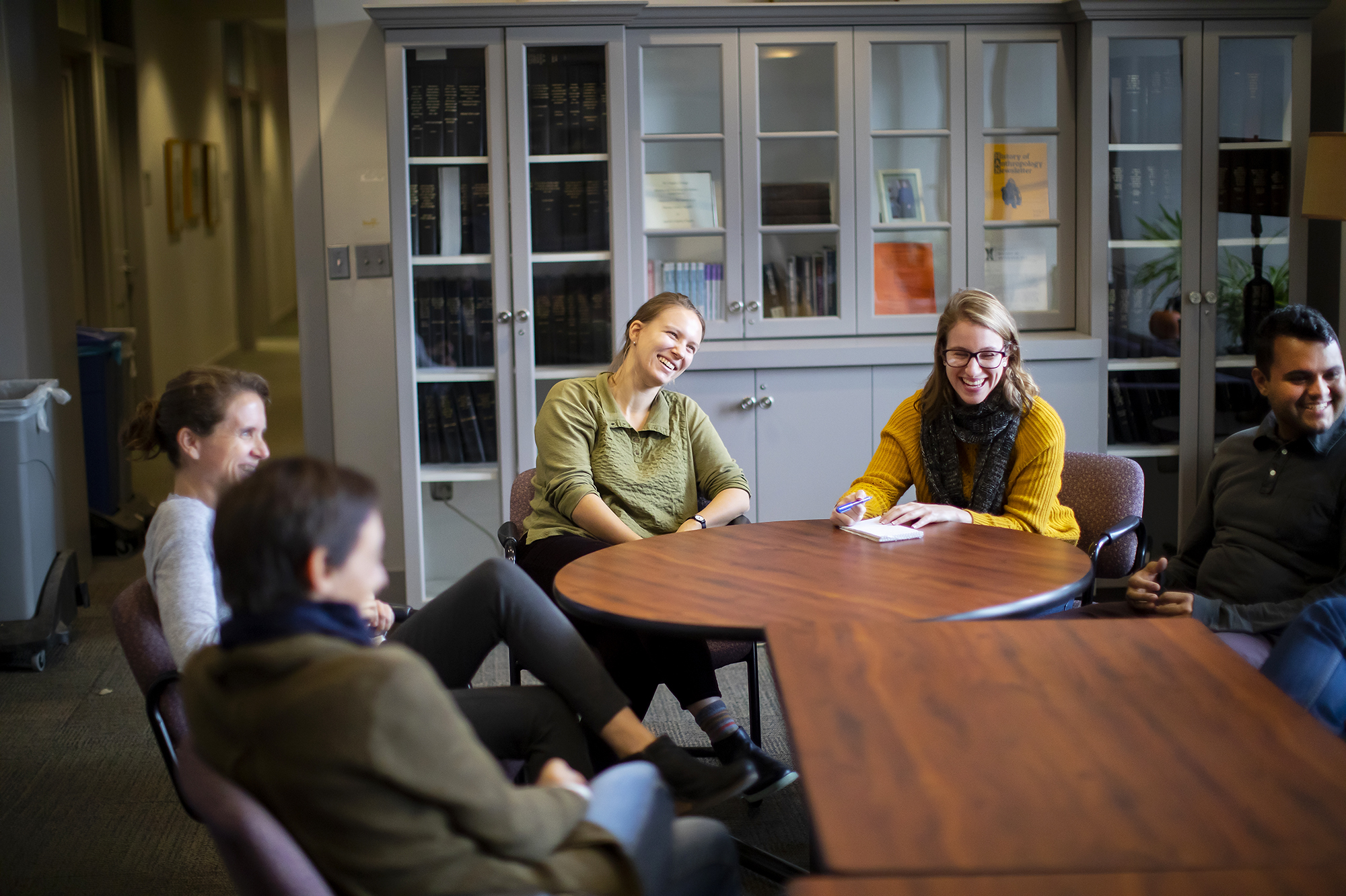 Five faculty members and graduate students seated around tables, talking and laughing