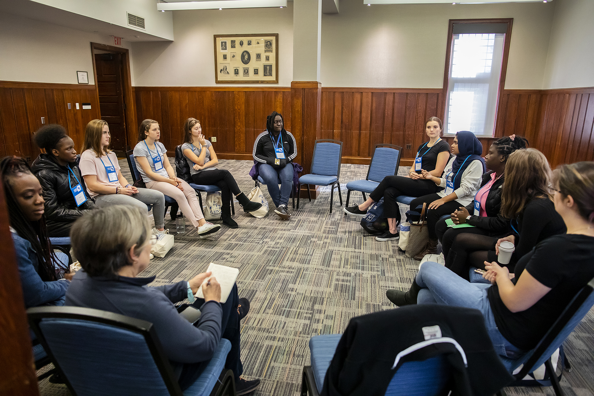 a group of people seated at a circle of chairs talking to each other