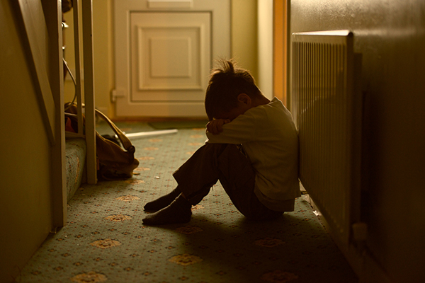 A young child sits in a hallway burying their head in their arms on a rather dirty carpet