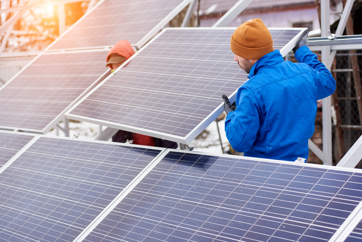 Two people installing solar panels on a chilly day, wearing gloves and snow hats. 