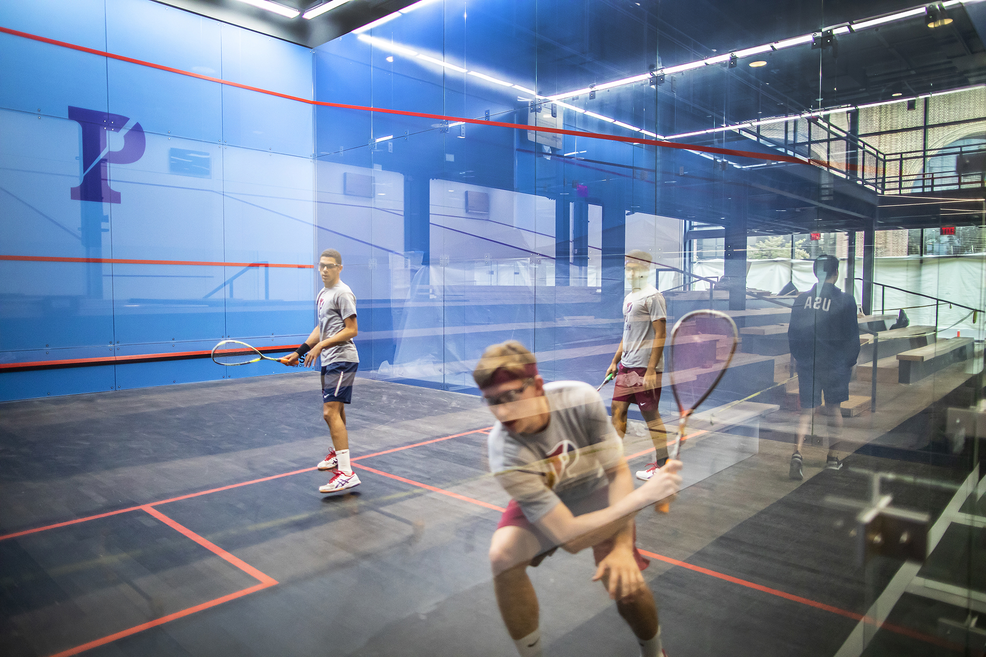 Three players practice in one of the glass courts at the new Penn Squash Center.
