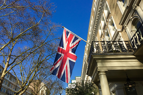 looking up at a Union Jack flag hanging from a balcony under a blue sky