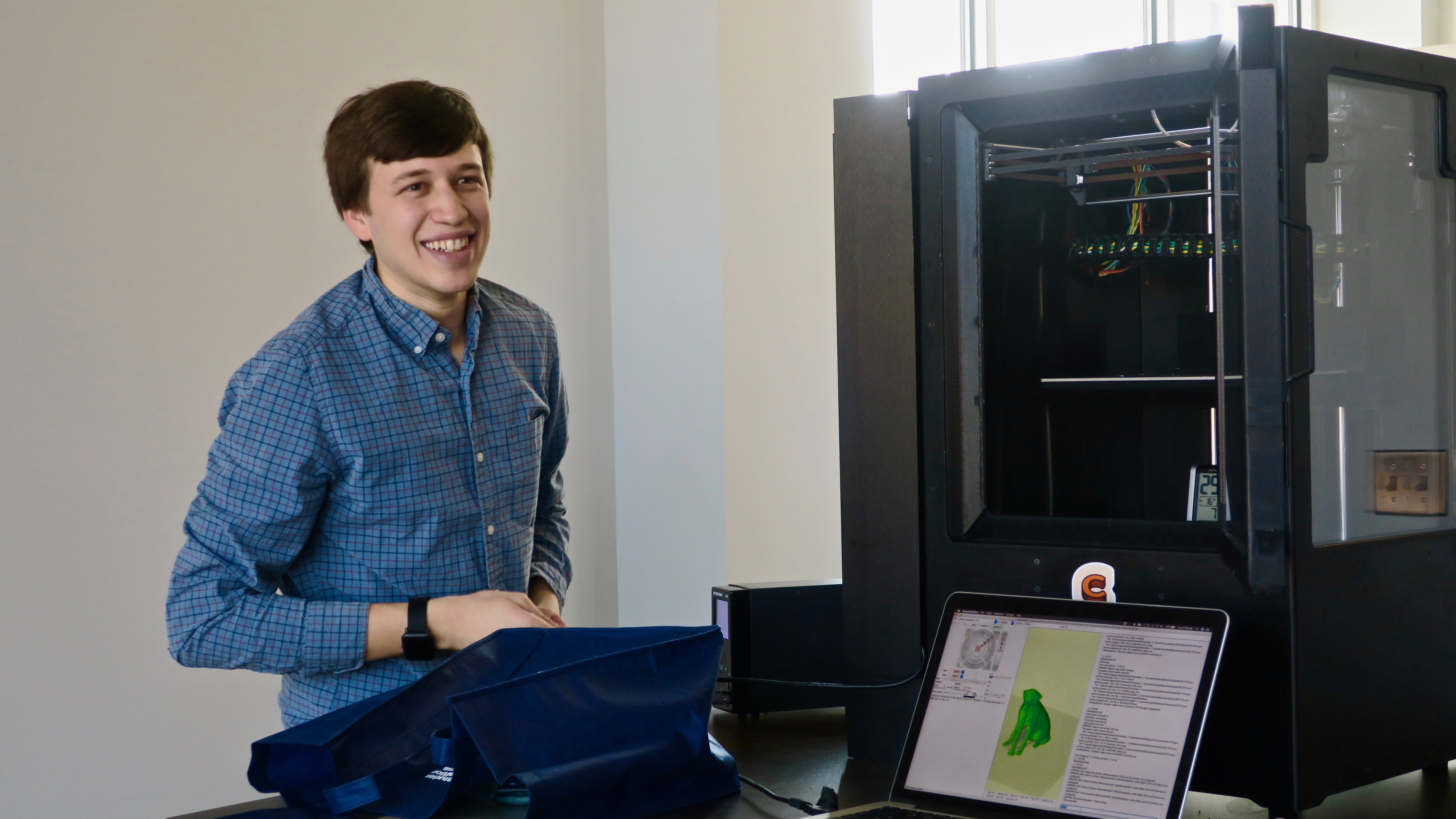 Evan Weinstein smiling beside his 3d chocolate printer and open laptop with a scan of a dog