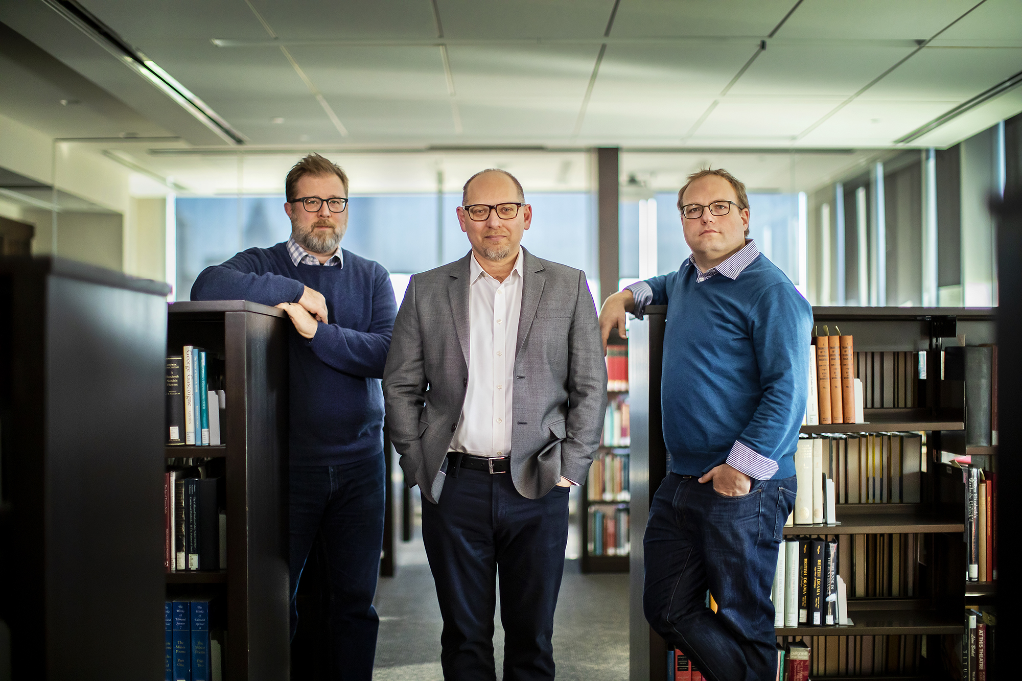 Three people standing in a library surrounded by bookshelves.