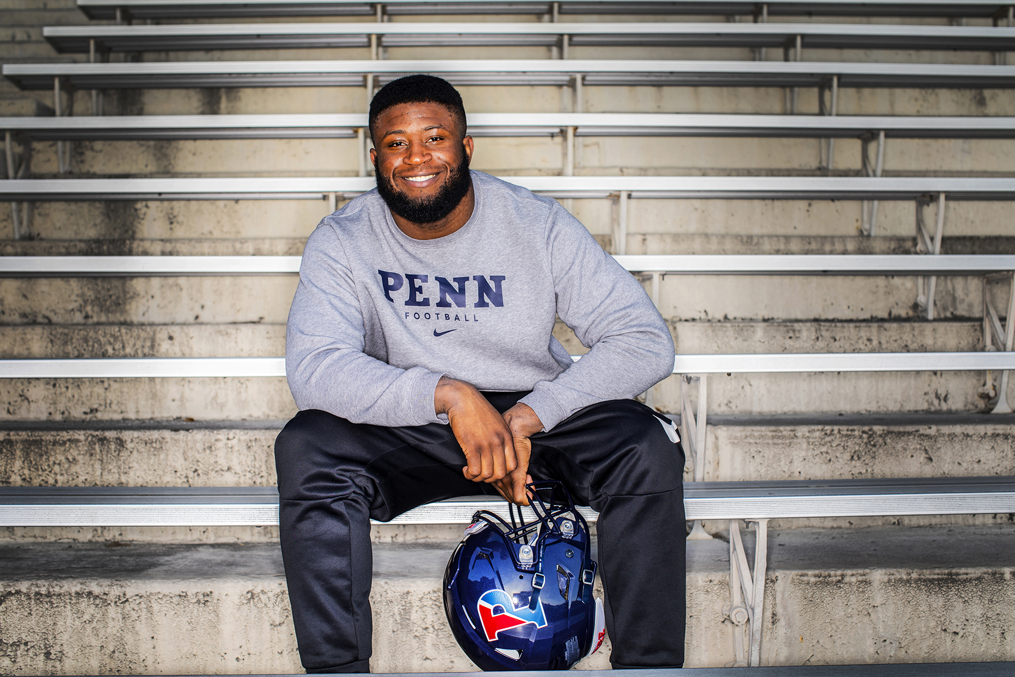Prince Emili of the football team sits in the Franklin Field bleachers with his helmet in his hand.