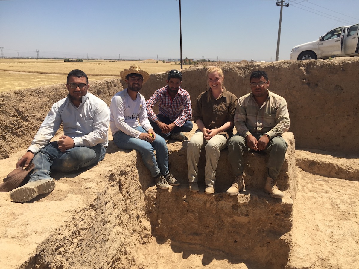 Five people sit along dusty mud walls on an archeological dig