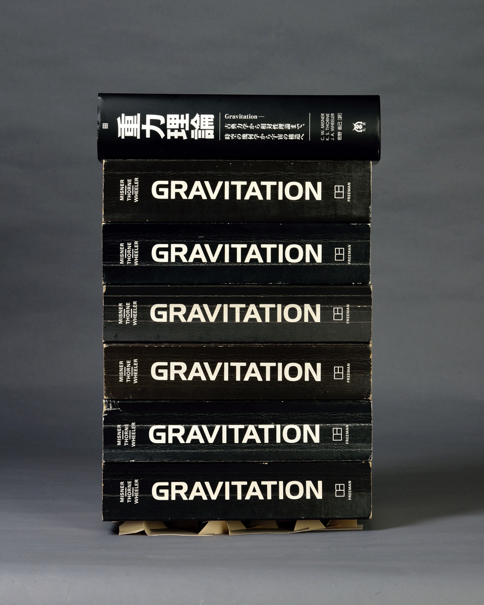 seven books with gravitation written on the spines, with one book in japanese, against a gray background on top of a small folded piece of paper