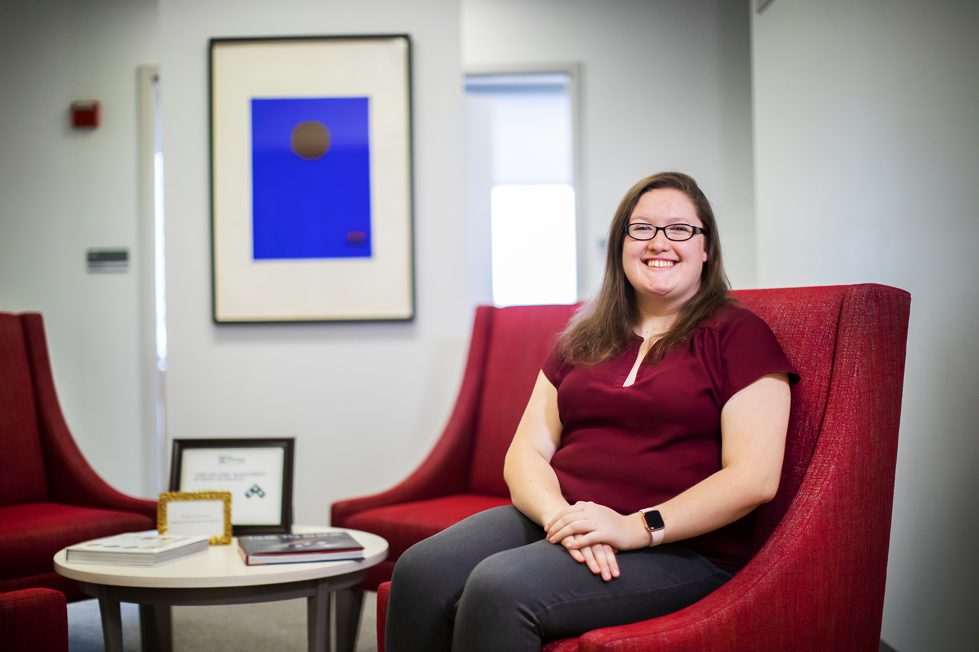 Woman with glasses sits in a lobby 