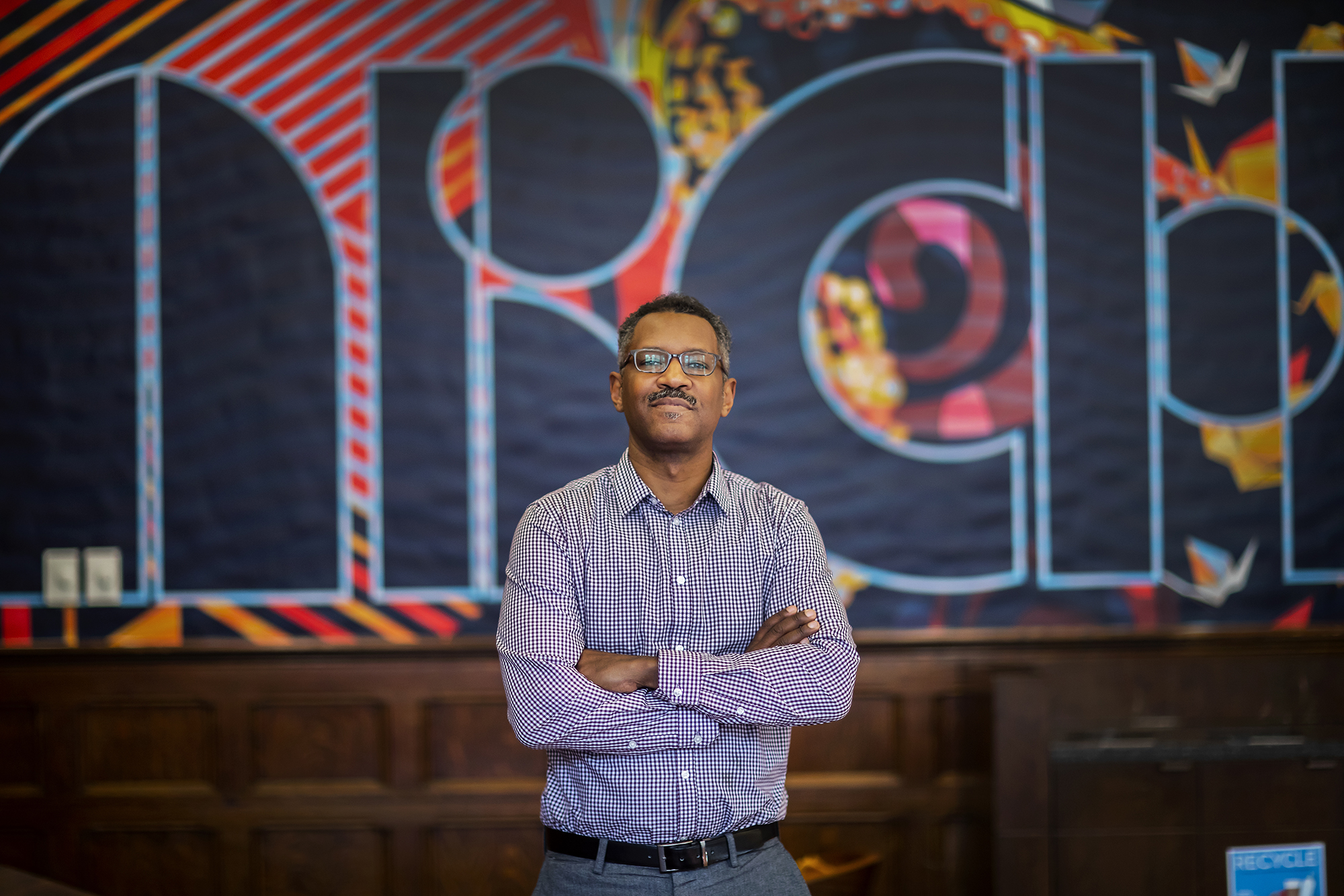 Man with crossed arms stands in front of a mural