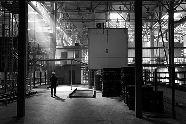 One factory worker in a hard hat walking alone on a factory floor.