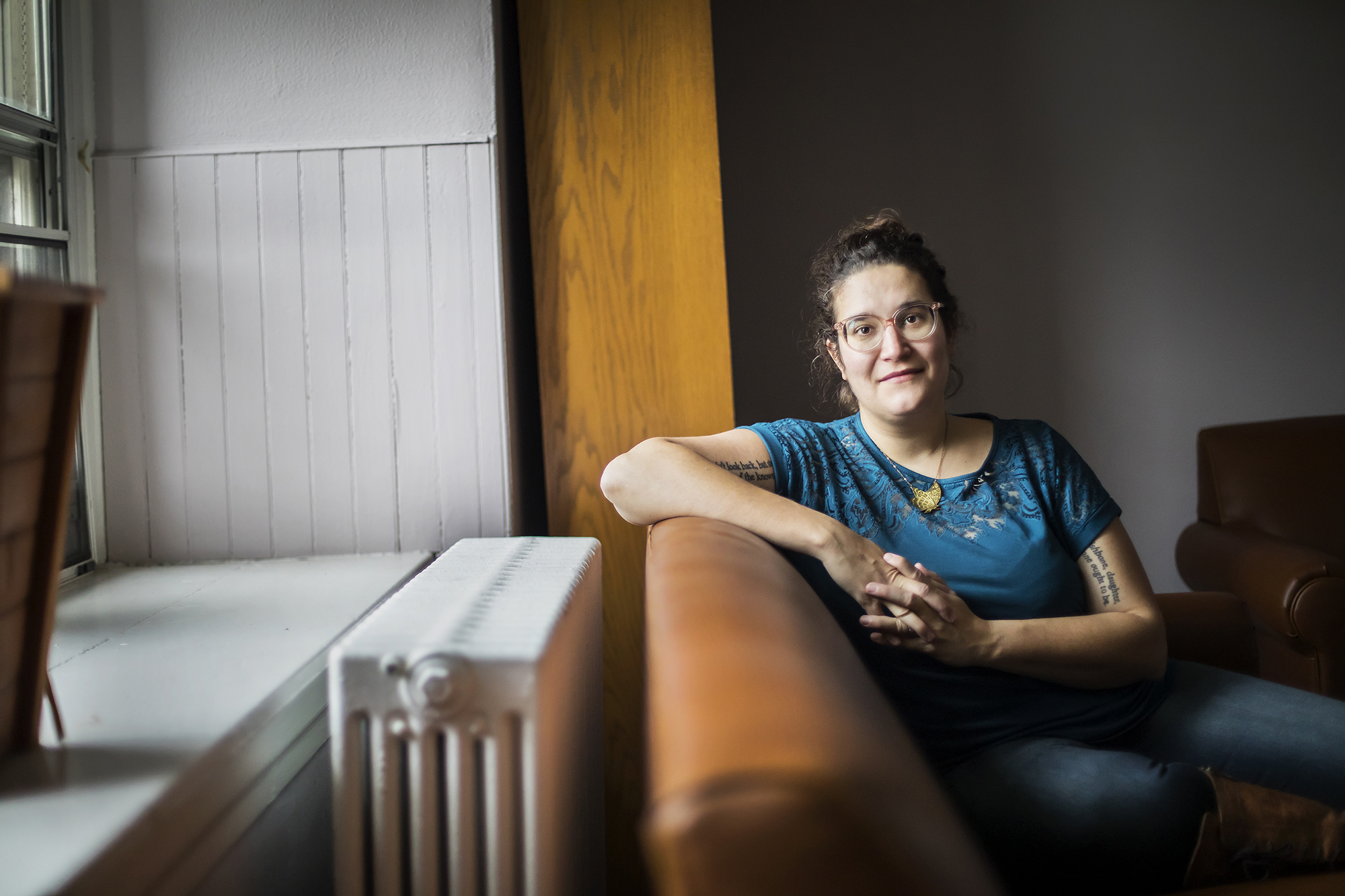 Author Carmen Machado sitting on a sofa near a window. 