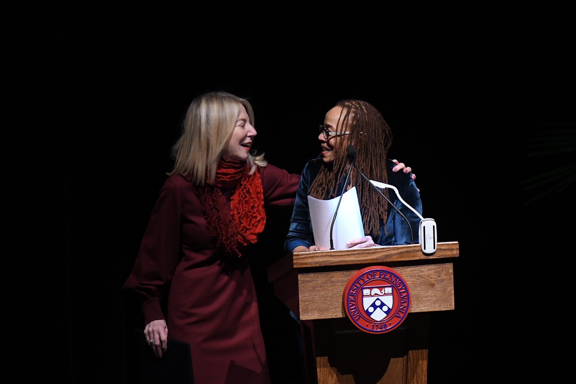 Penn President Amy Gutmann puts her arm around Dorothy Roberts shoulder who is at a University of Pennsylvania podium