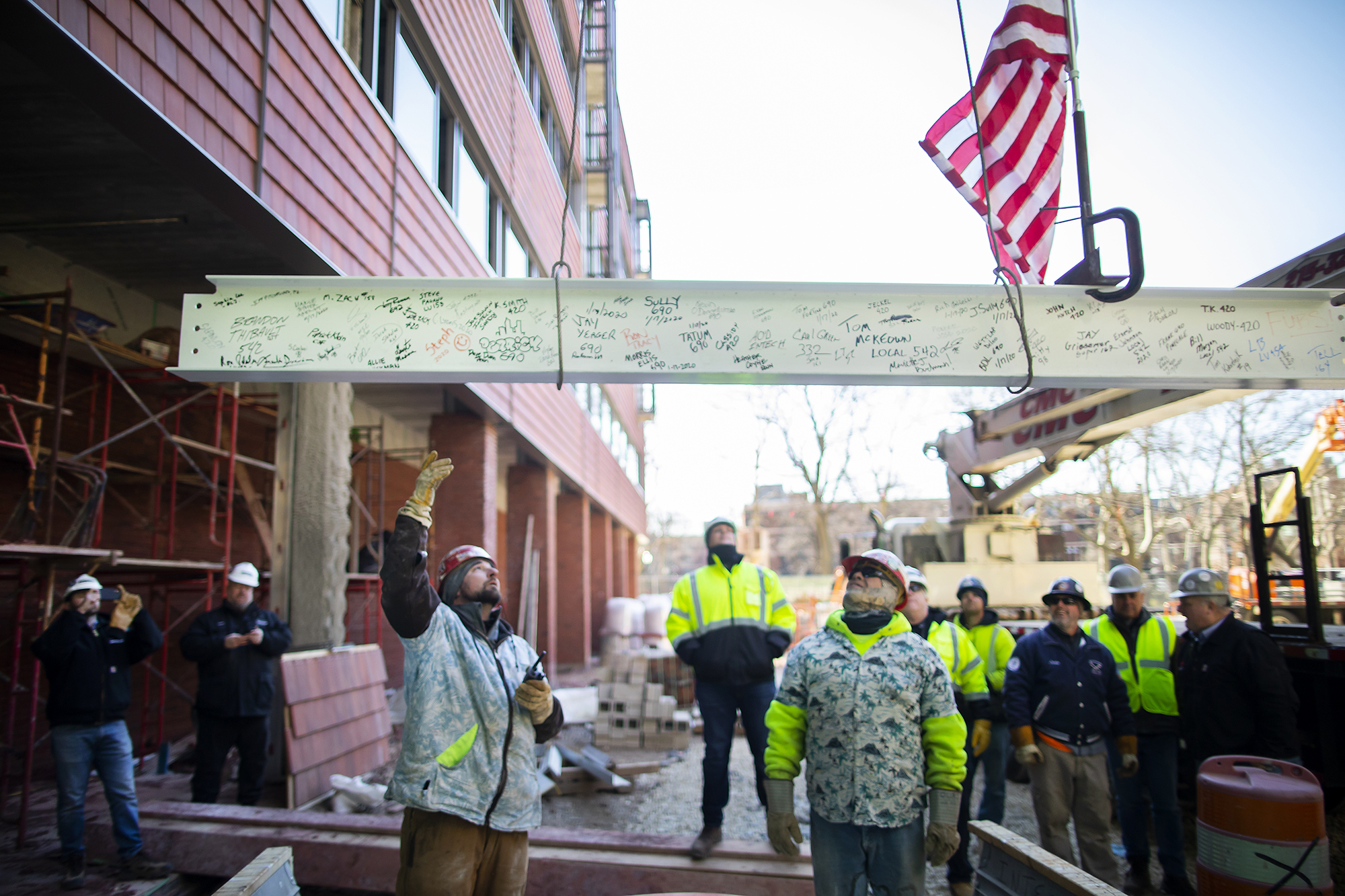 Two construction workers watch as the final beam is hoisted up via crane 