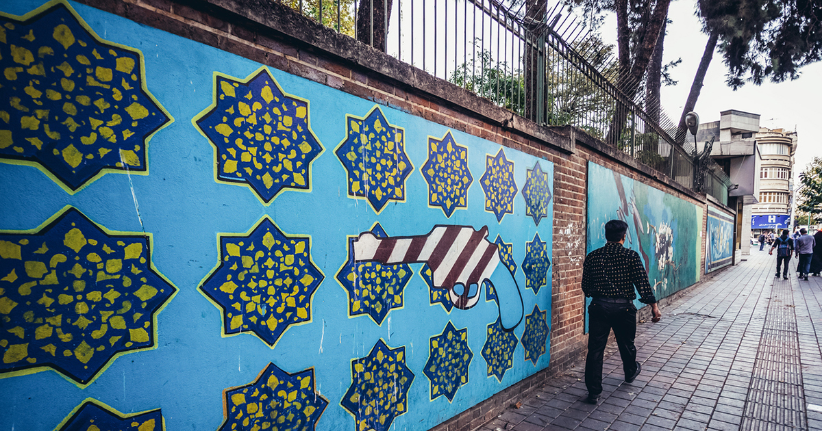 Pedestrian on the sidewalk walking past the wall of the former US embassy in Tehran.