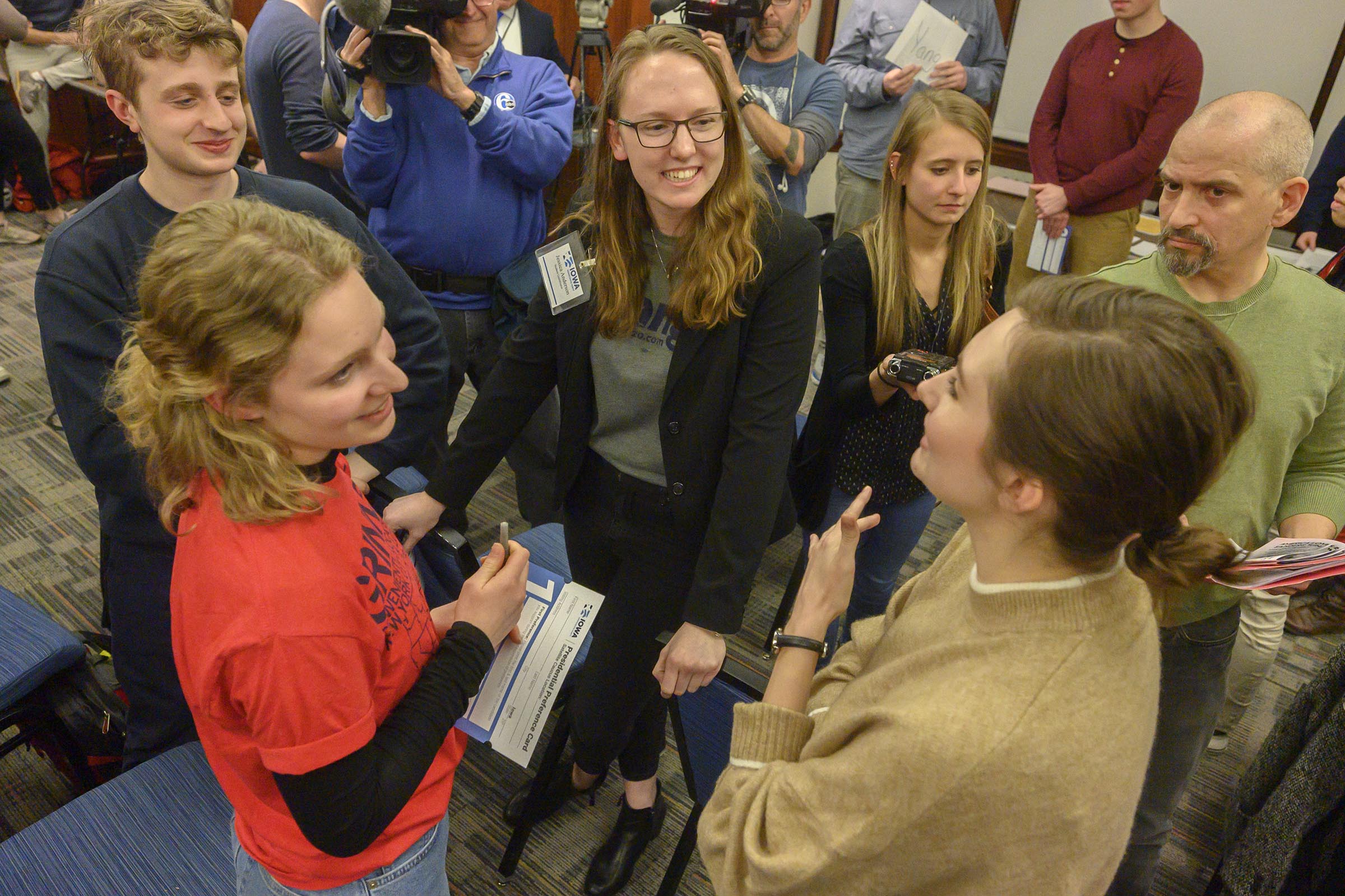 A group of people talking and laughing in a cluster, with a video camera being held in the top left corner. 