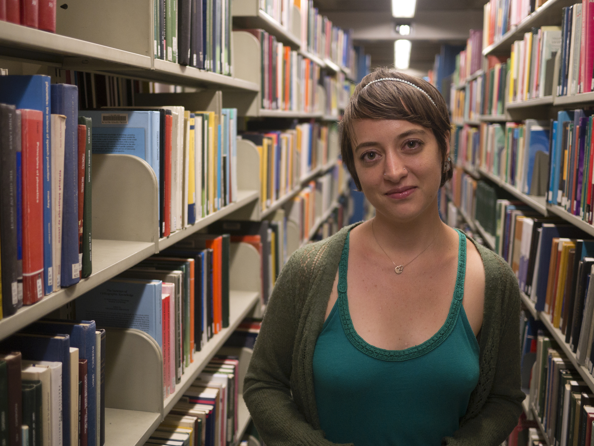 A person standing in a library stack, with shelves of books on either side. 