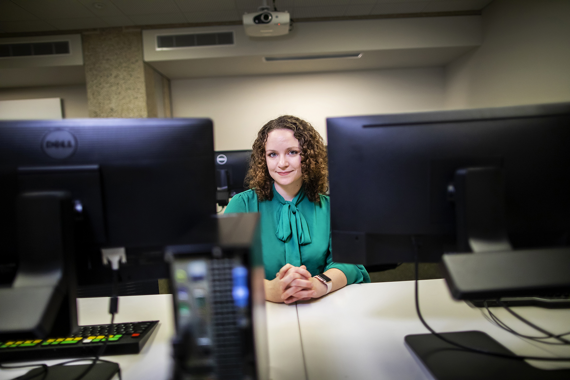 Person sitting with hands folded behind a bank of computer monitors