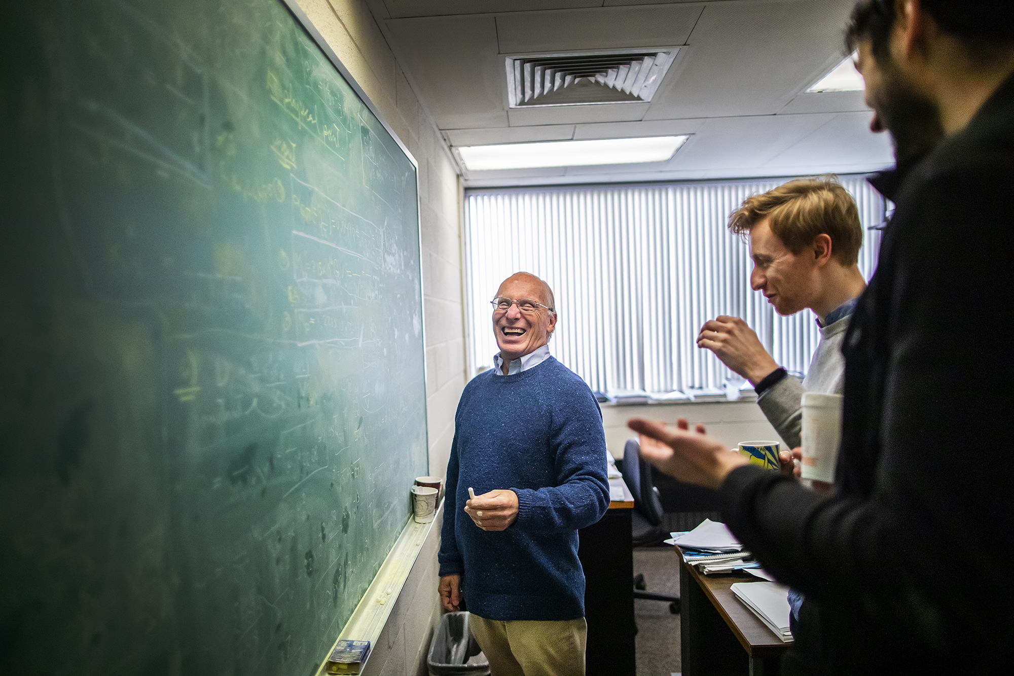 three people in front of a chalk board, the person closest to the board is laughing