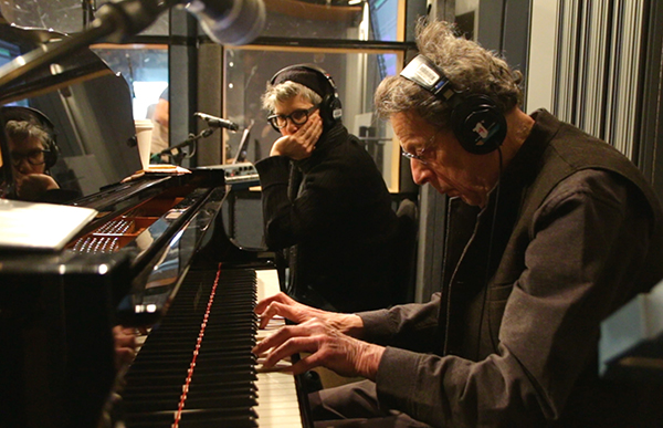 Philip Glass at piano wearing headphones
