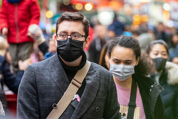 Two people outside in a public crowd wearing face masks