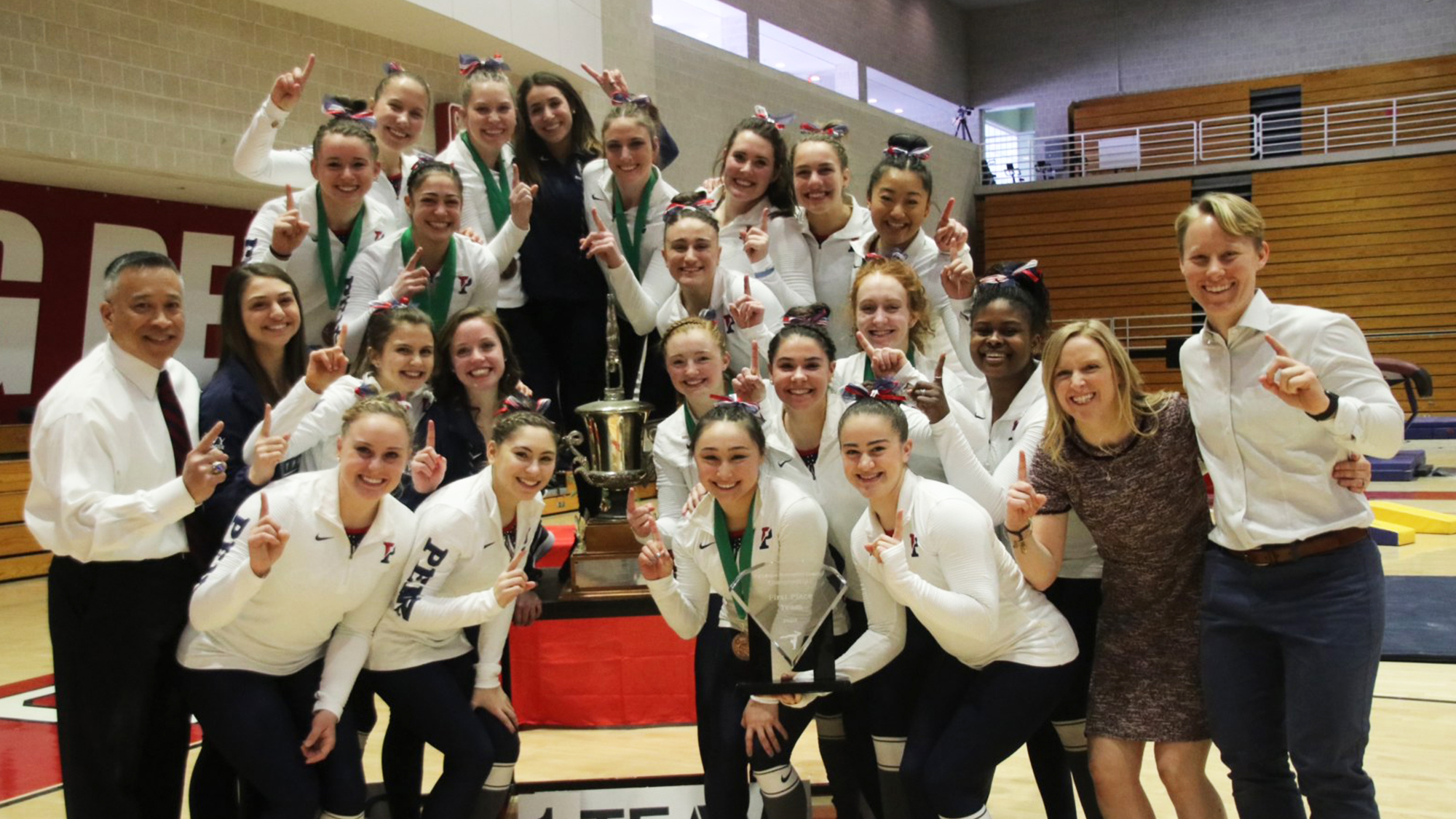 Coaches and players on the gymnastics team hold up the No. 1 finger after winning the Ivy Classic.