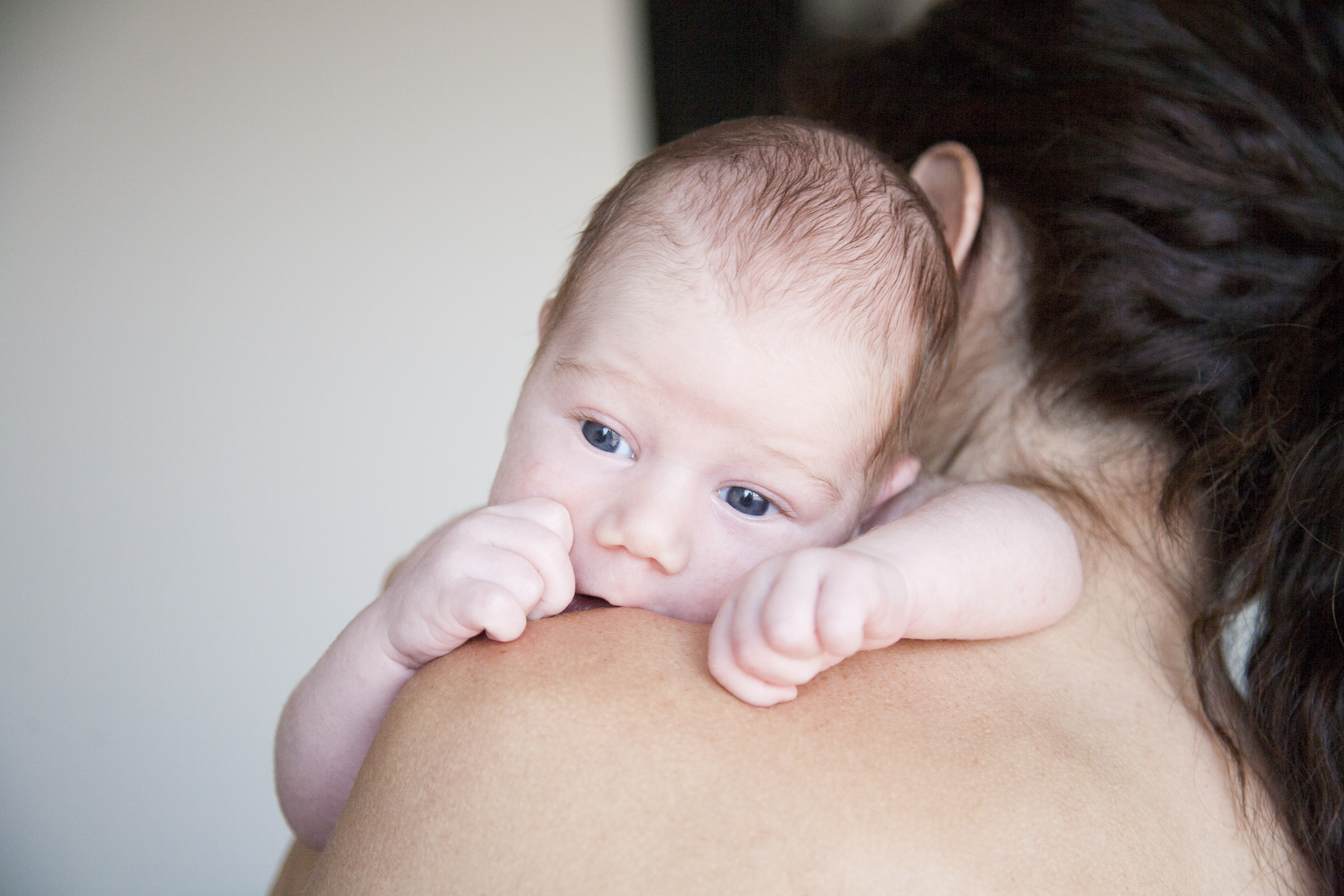 A young baby in only a diaper being held over another person's shoulder, which is bare. 
