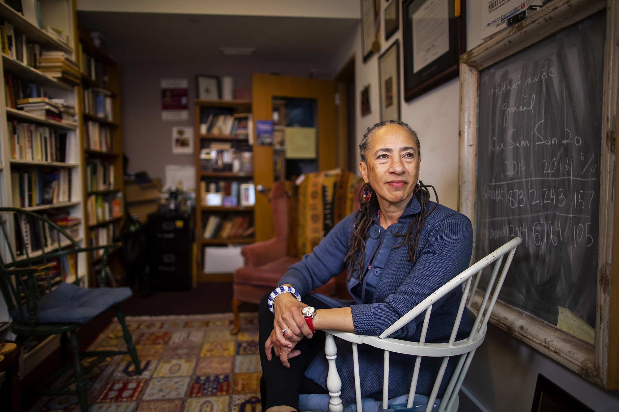 Lorene Cary seated in a chair in her office next to a blackboard