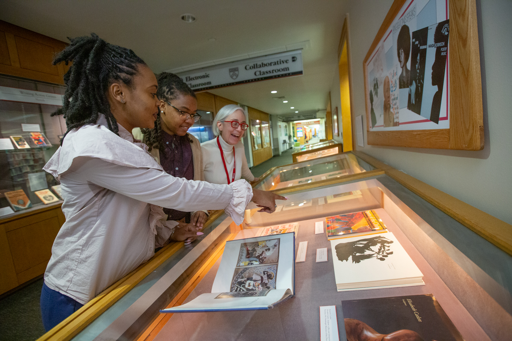 Two graduate students and library curator looking at the Joanna Bank Exhibit at Library