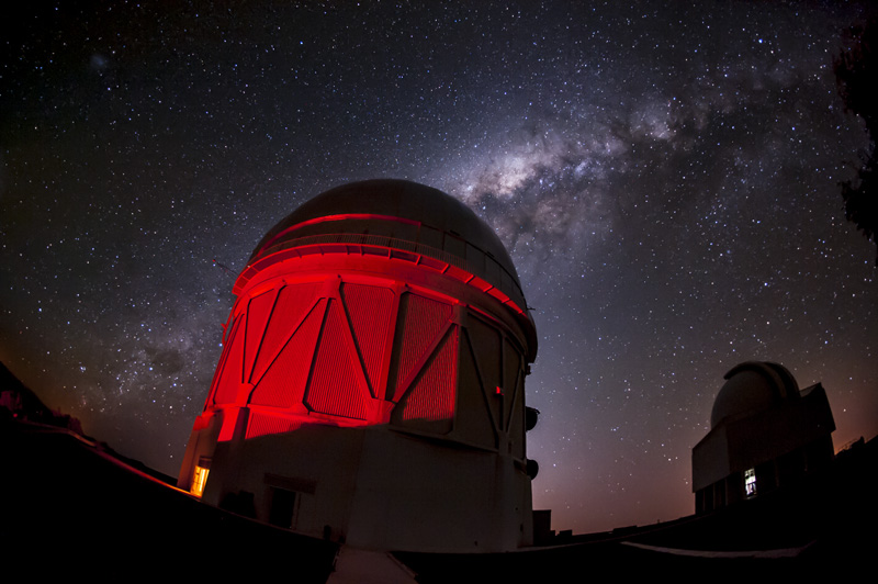 a telescope dome bathed in red light with the milky way galaxy behind it