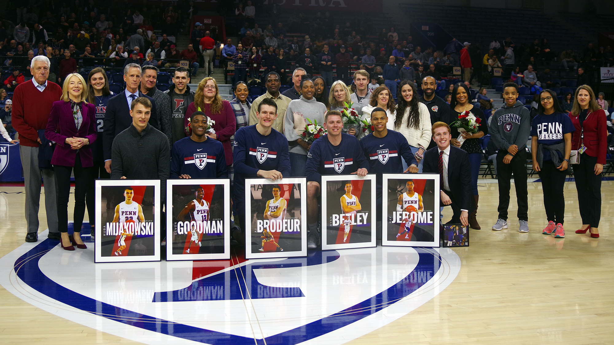 President Gutmann and others stand on the court with winning Penn basketball team holding their player posters 