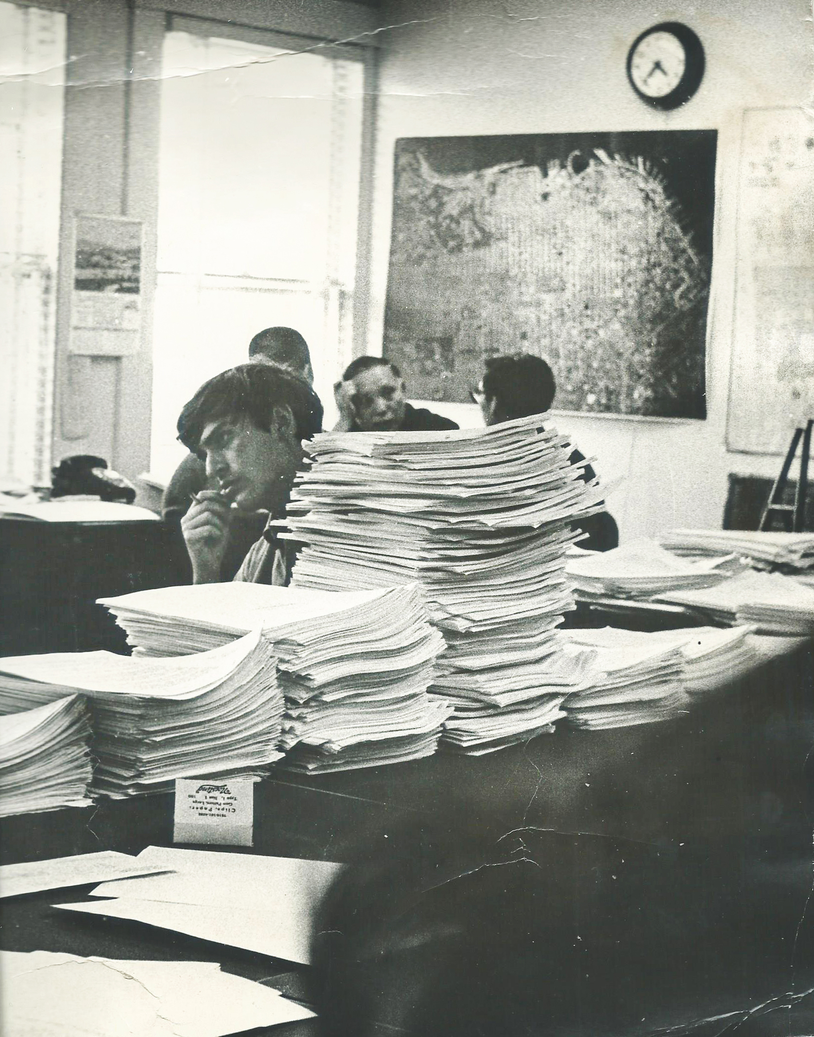 A person sits behind stacks of papers.