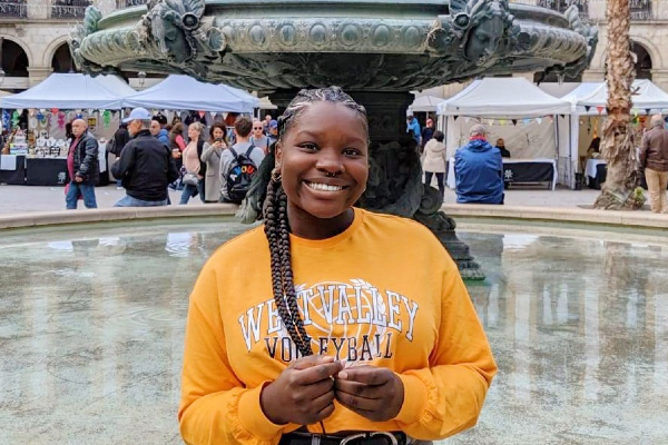 Student standing in front of an outdoor fountain. 