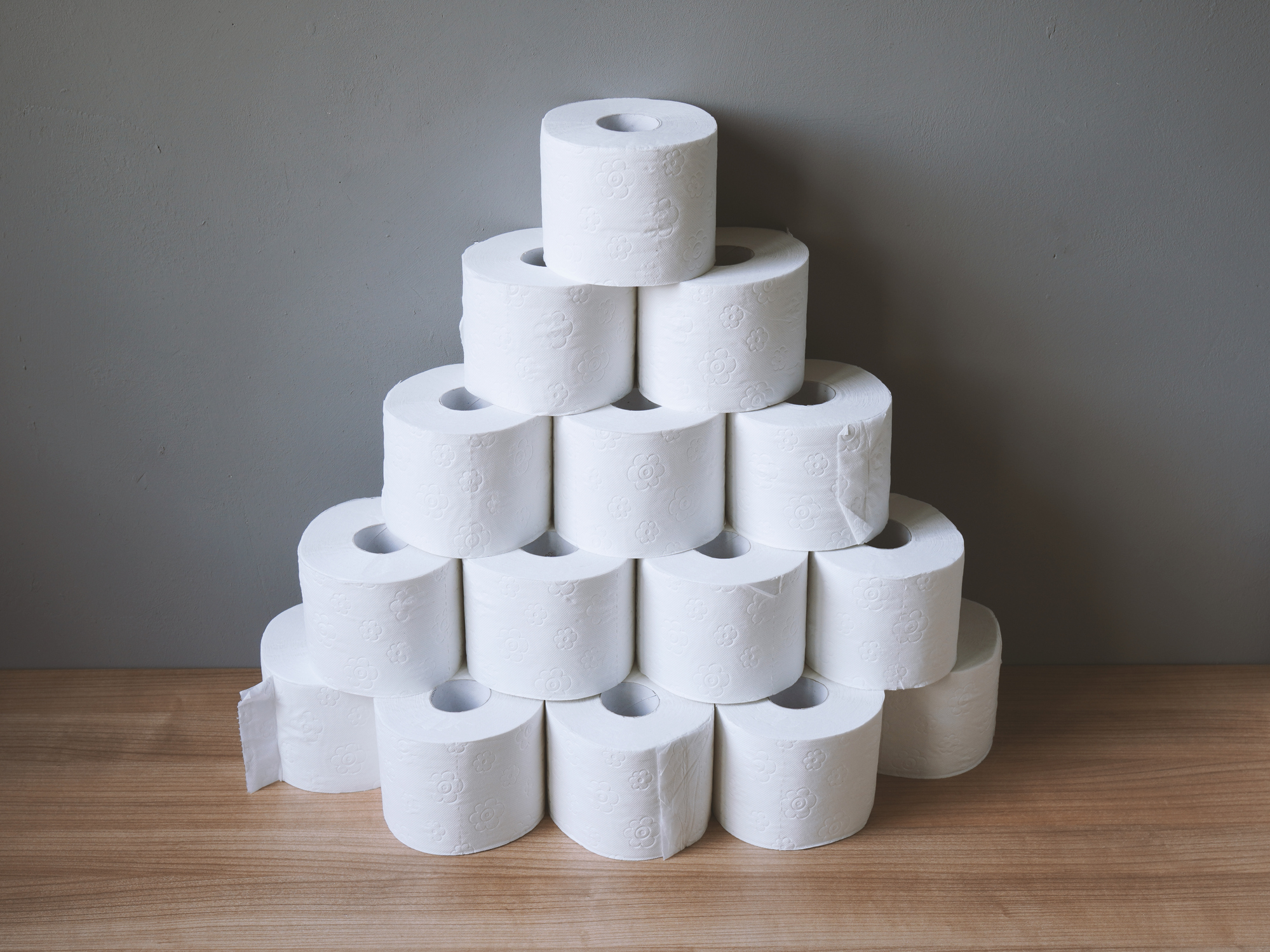 A pyramid made up of rolls of toilet paper on a wooden tabletop. 