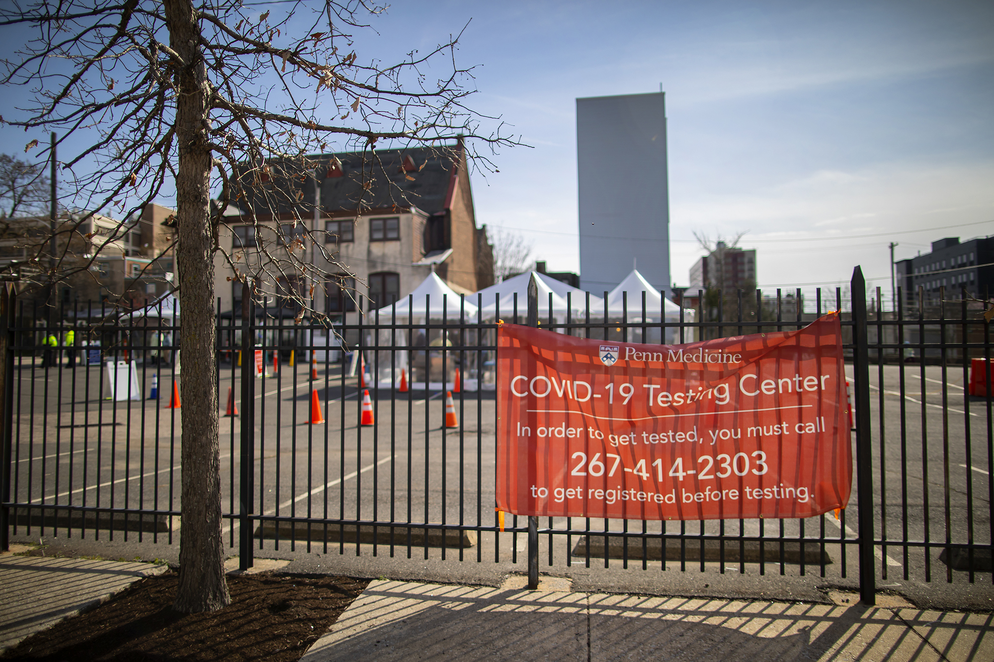 A parking lot  in daylight with a sign on the front gate reading Penn Medicine COVID-19 Testing Center