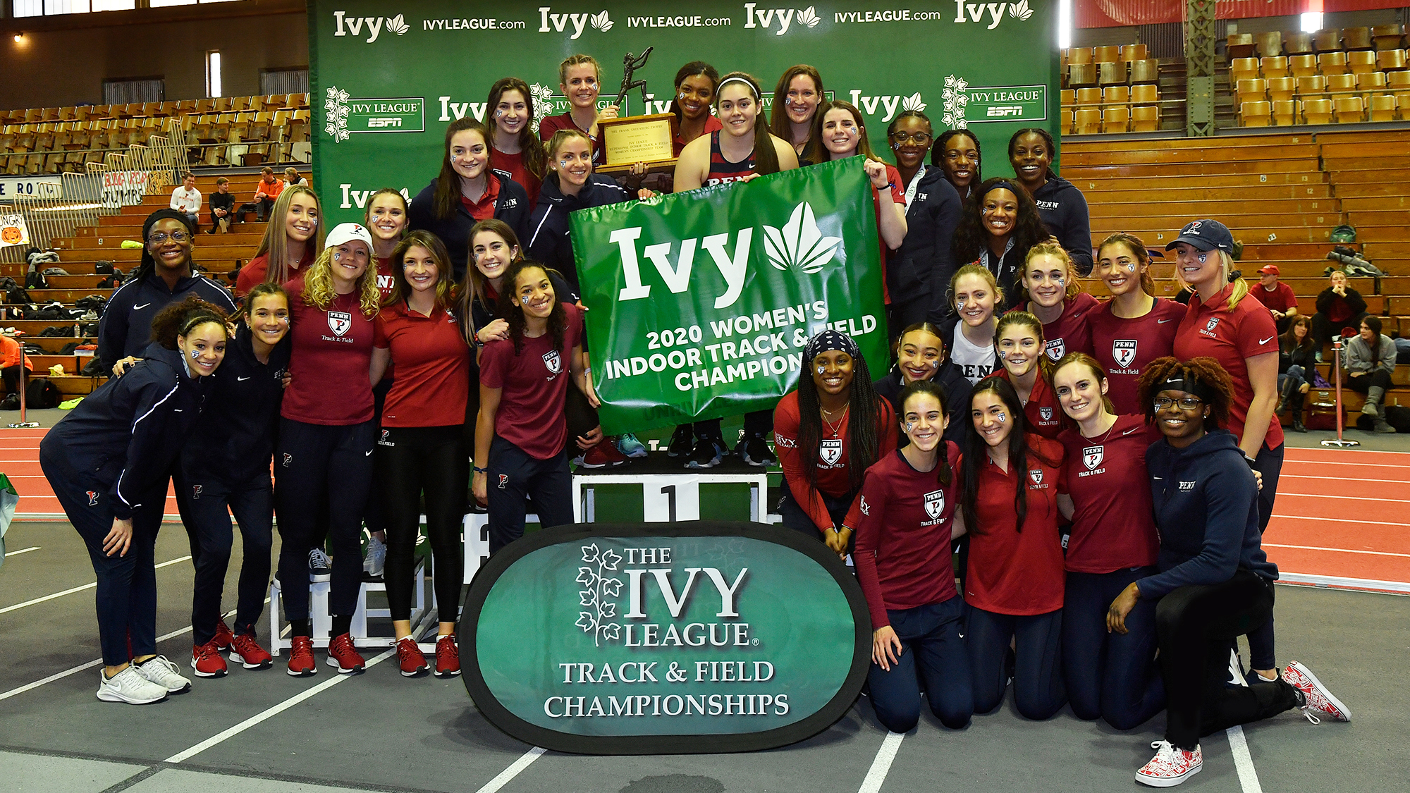 Members of the women's track and field team pose with a championship banner after winning the Indoor Ivy Heps.