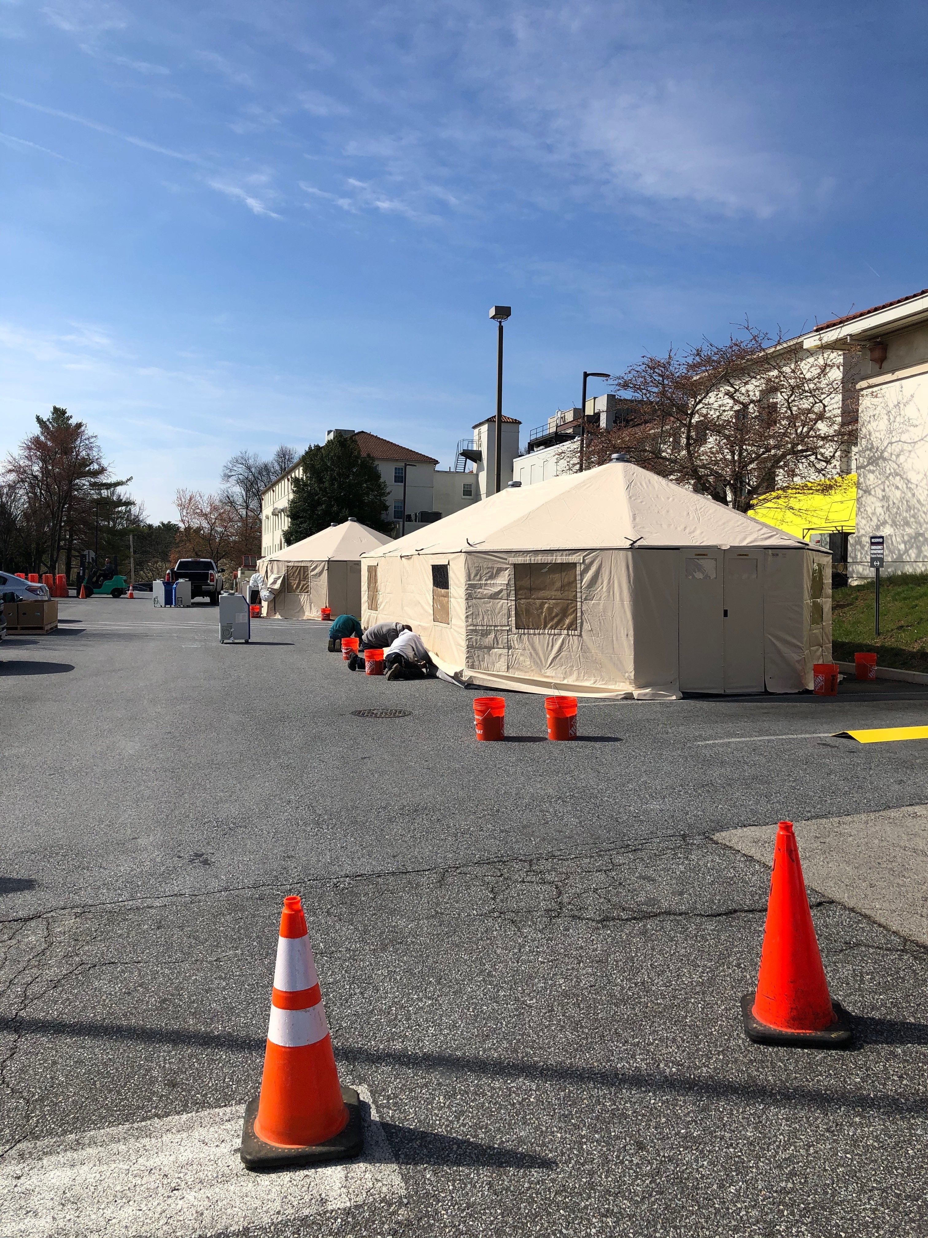 Temporary tents in a parking lot, with some neon orange cones and several neon orange buckets.