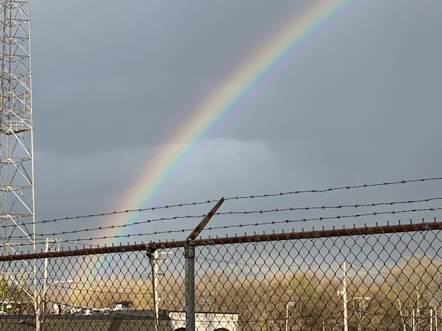 A rainbow arches above a barbed wire fence