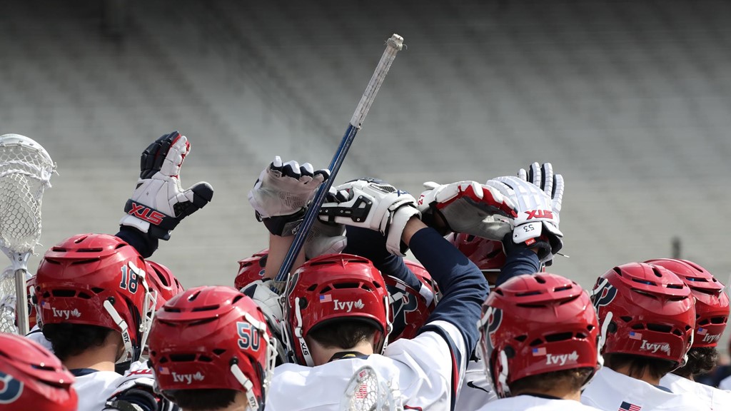 Men's lacrosse players put their hands up and together in a huddle.